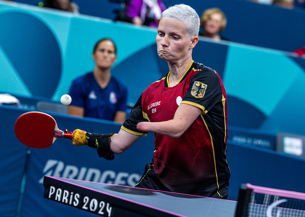 Paralympian Thomas Schmidberger competes in a table tennis match at Paris 2024, wearing a sports uniform, as a referee looks on