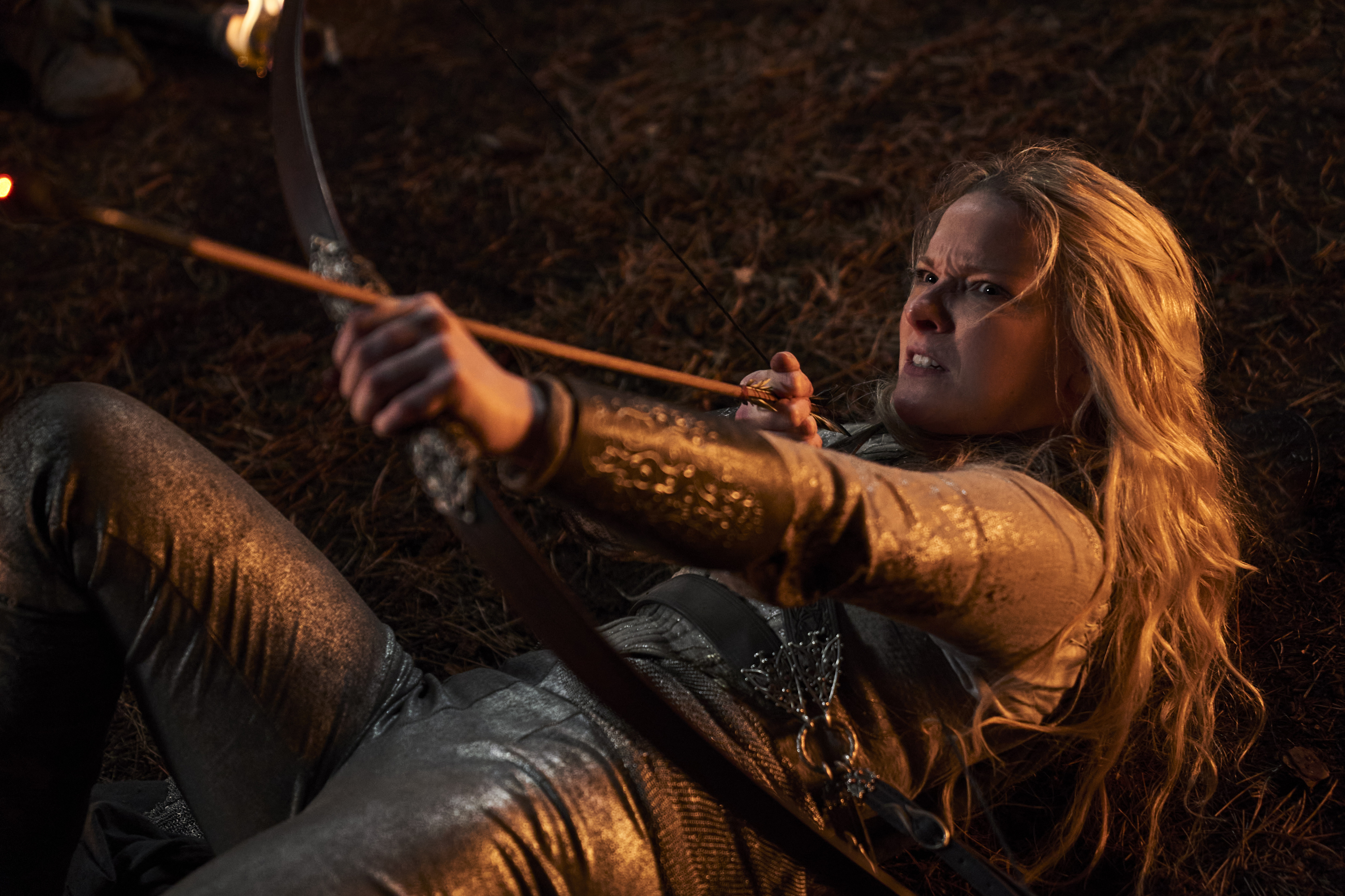 Morfydd Clark as Galadriel lying on her back and aiming an arrow in a scene from "Lord of the Rings: The Rings of Power"