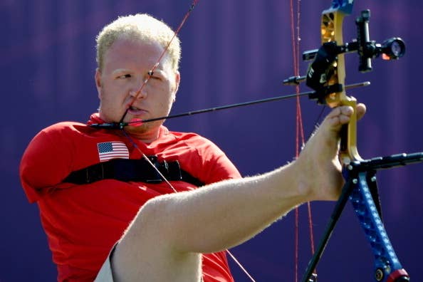 An archer pulls back his bowstring using his mouth and left foot. He competes in adaptive archery, underscoring his determination and skill