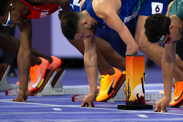 Track and field athletes, including Cuba's Roger Iribarne on the left, at the starting blocks during a race. One holds a brightly colored relay baton