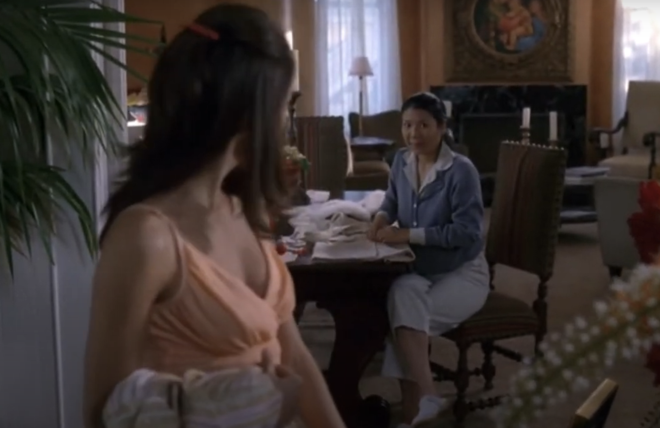 Eva Longoria stands holding laundry, looking at Judy Reyes, who is sewing at a table in a well-furnished room