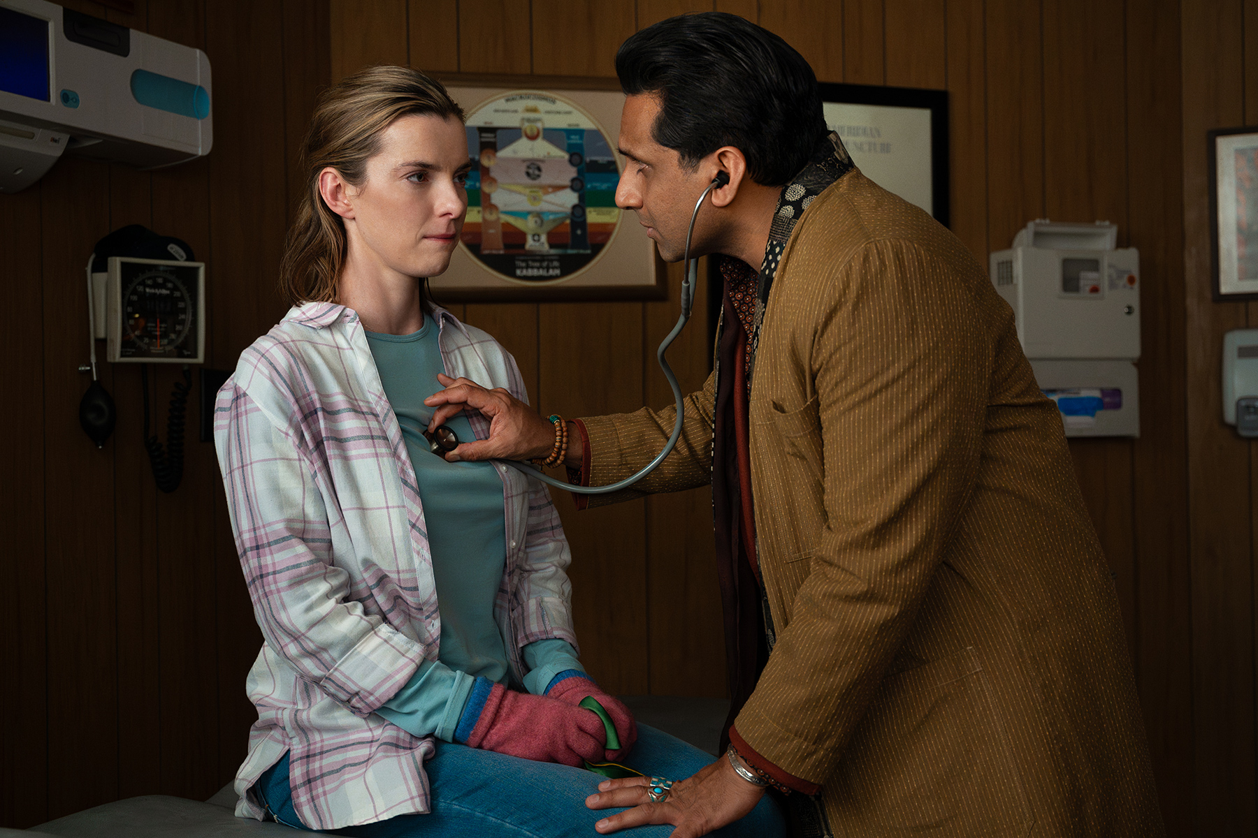 Betty Gilpin in a doctor's office, with a man listening to her heart with a stethoscope in a scene from "Three Women"