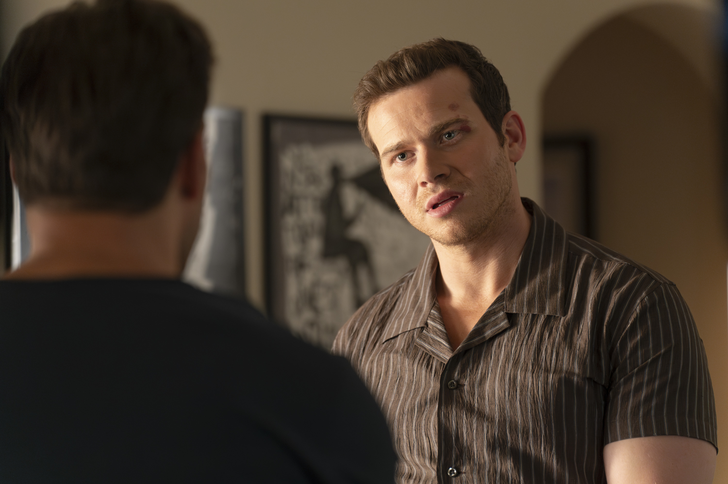 Oliver Stark and Ryan Guzman in a room, engaged in a serious conversation. Oliver is facing Ryan, showing concern