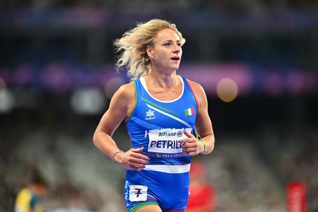 Valentina Petrillo runs on a track during a sports event, wearing athletic uniform with her name on it