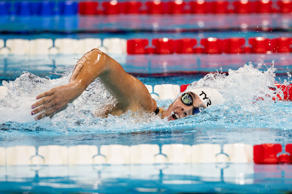Anastasia Pagonis in the middle of a freestyle race is seen at an indoor swimming pool, demonstrating a powerful stroke