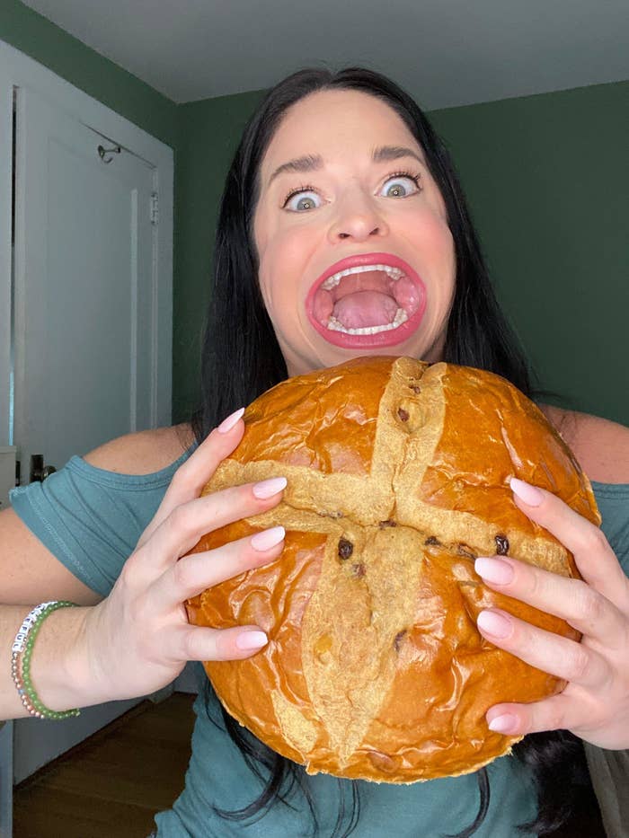 Woman with a surprised expression holding a large round bread with a cross shape on it