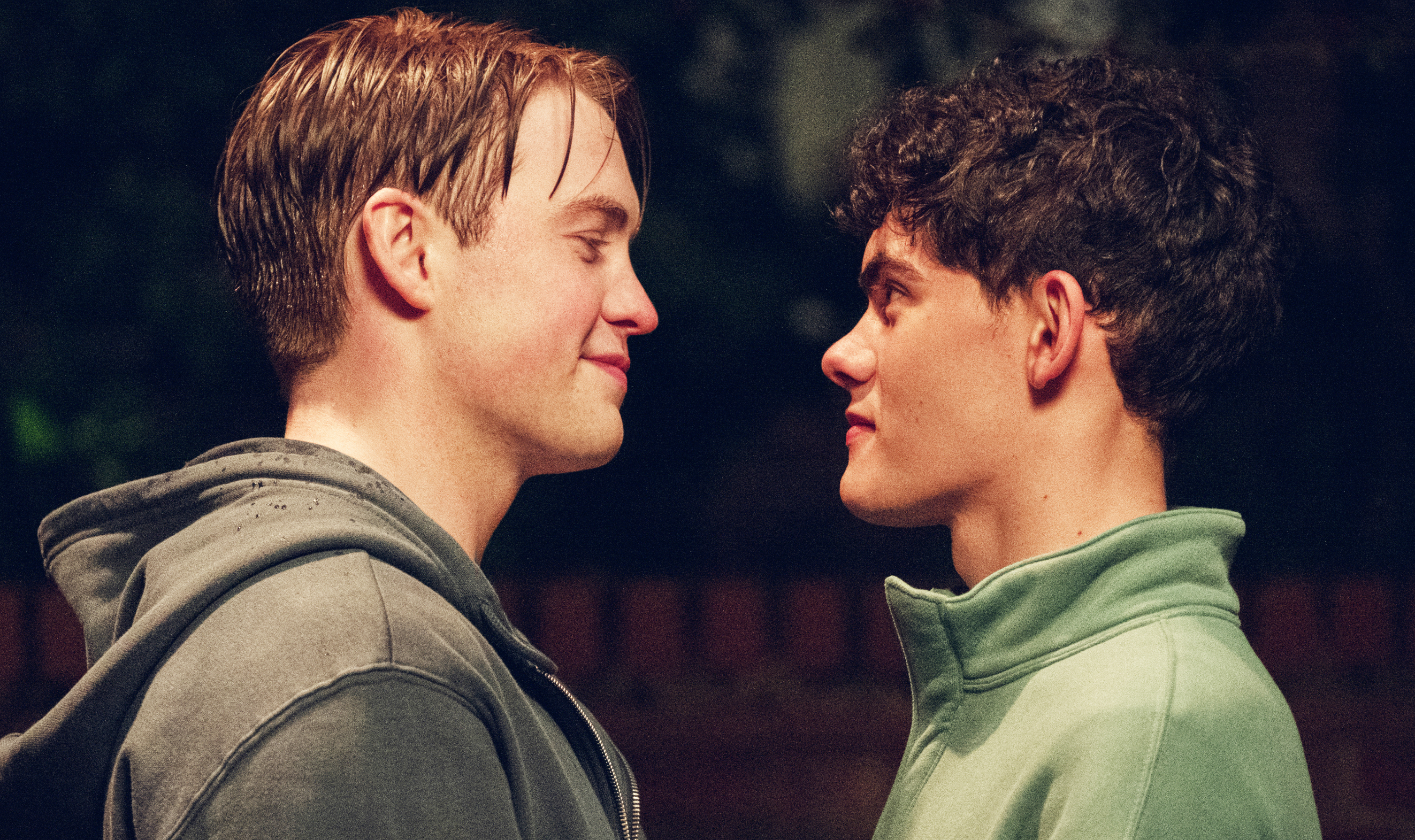Two people, Kit Connor and Joe Locke, facing each other and smiling, outside at night