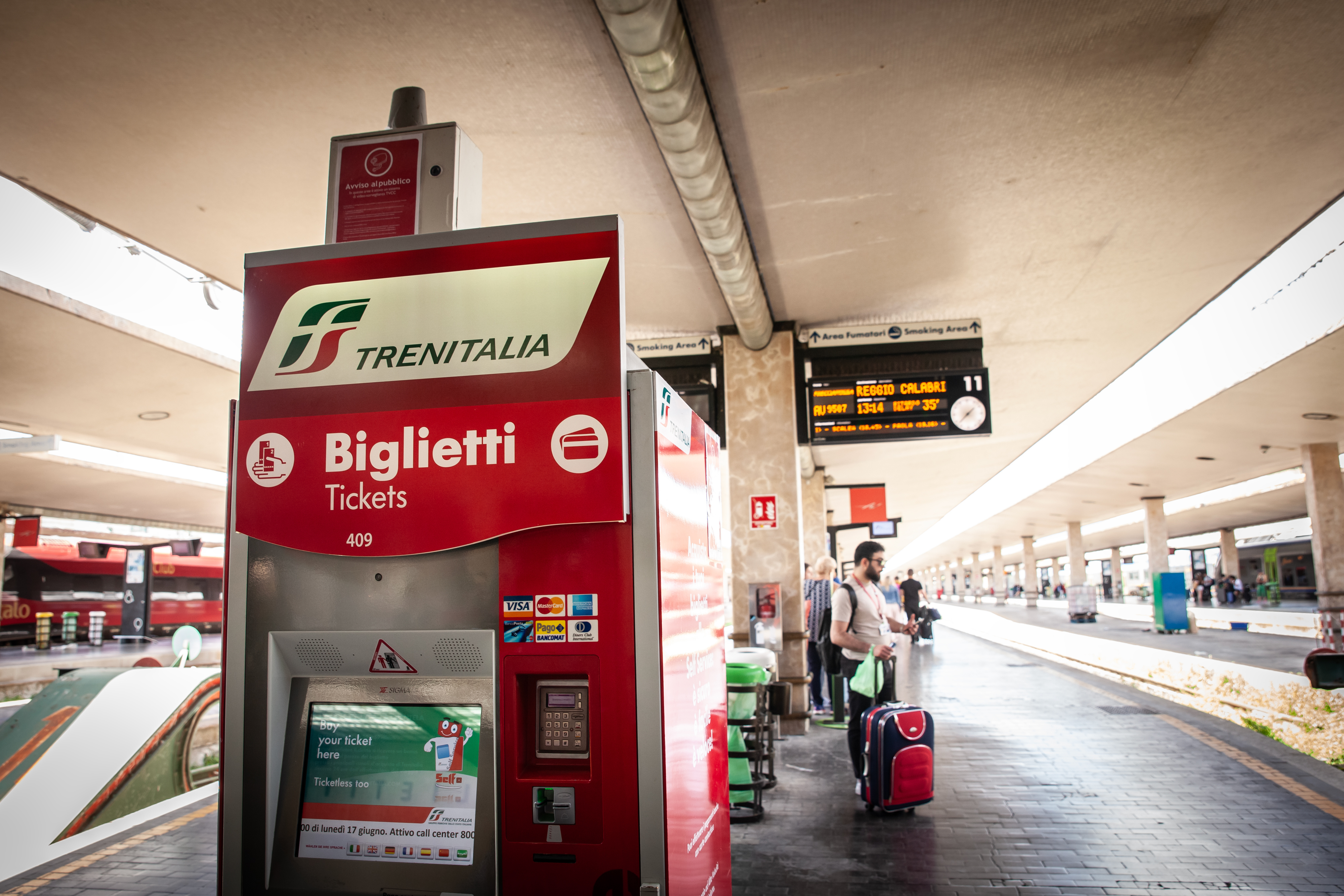 Trenitalia ticket vending machine in a train station; people standing in the background