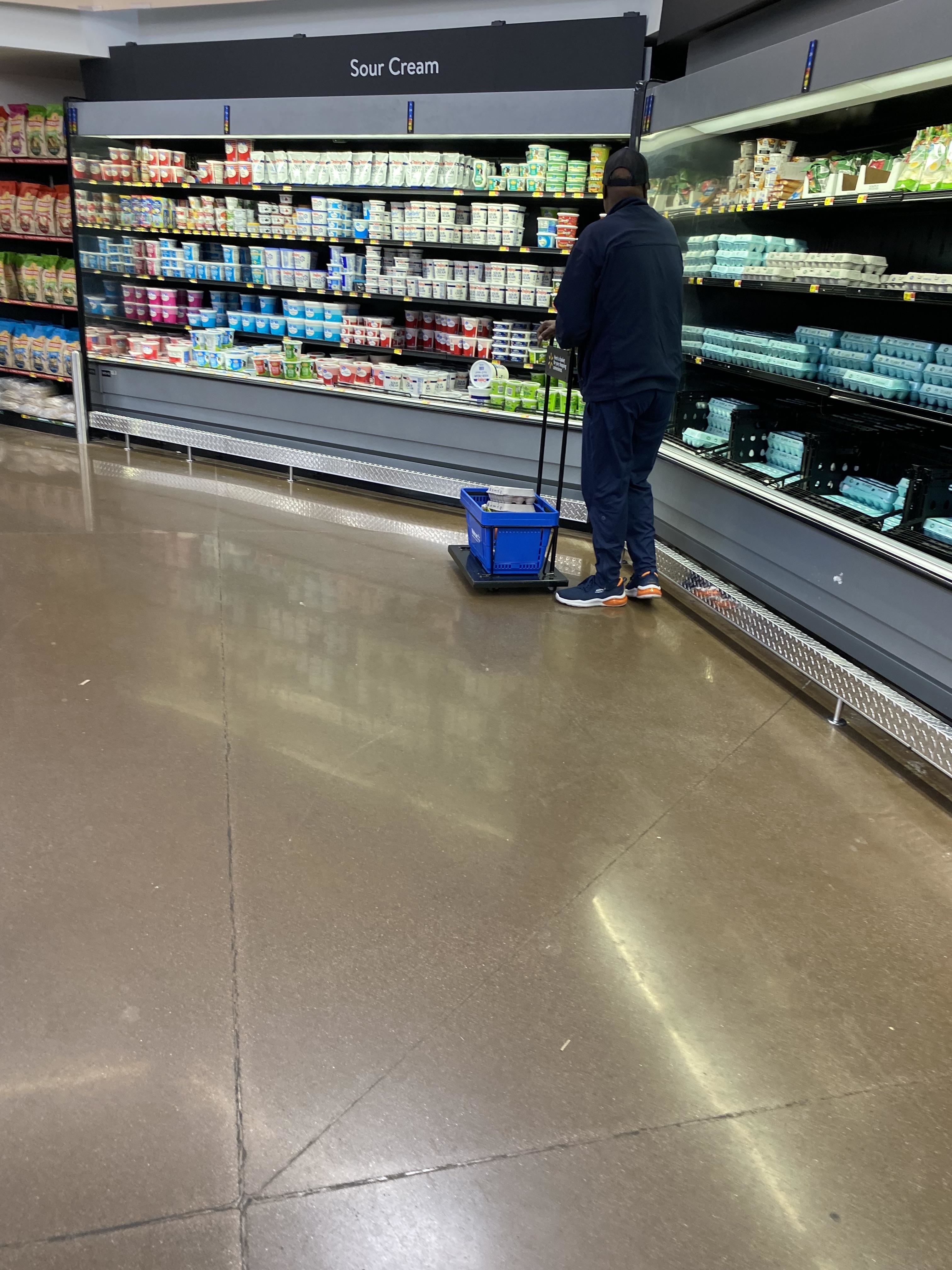 Person in a grocery store shopping for dairy products, facing away and pulling a blue basket