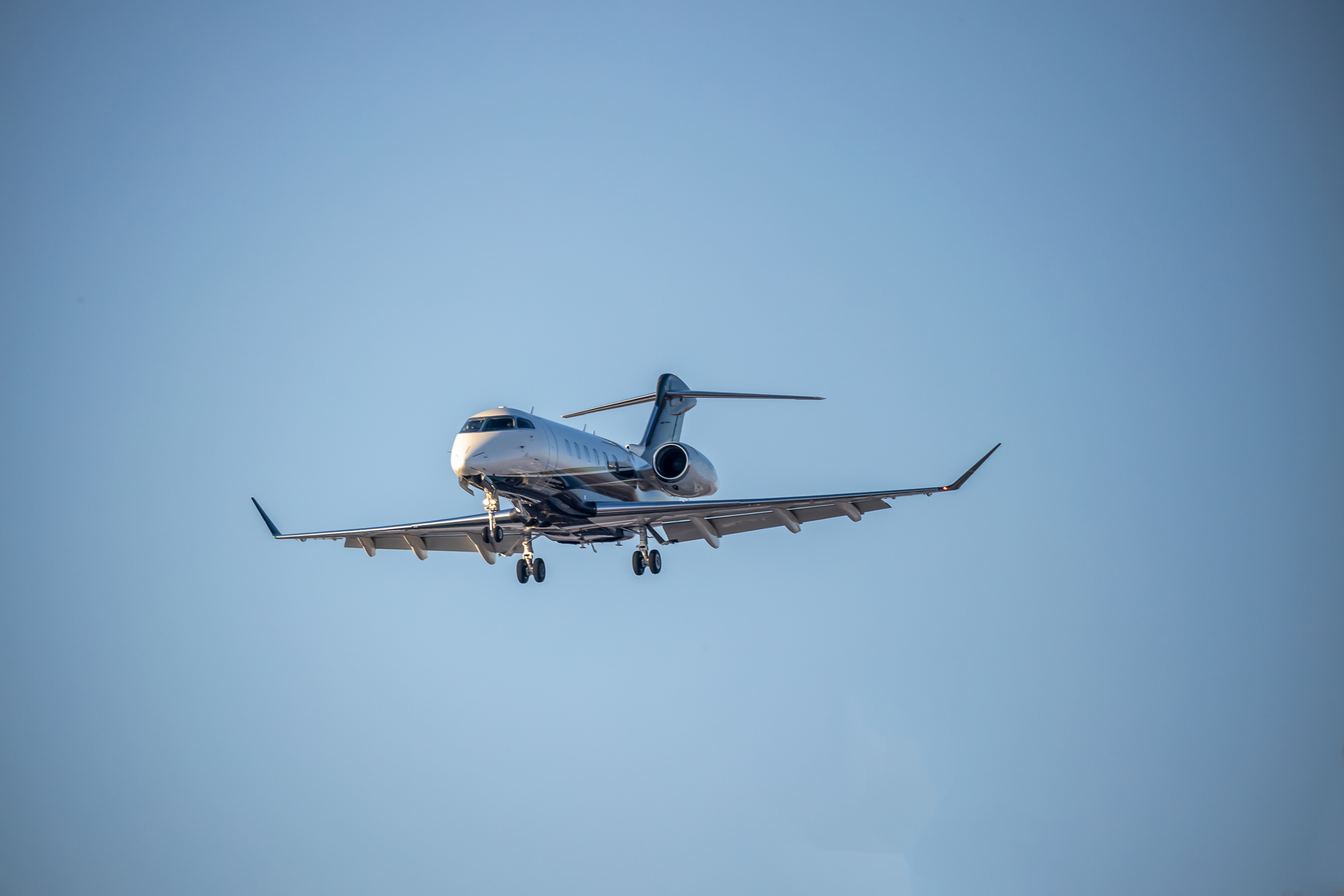 A private jet aircraft is in flight against a clear sky, approaching for a landing