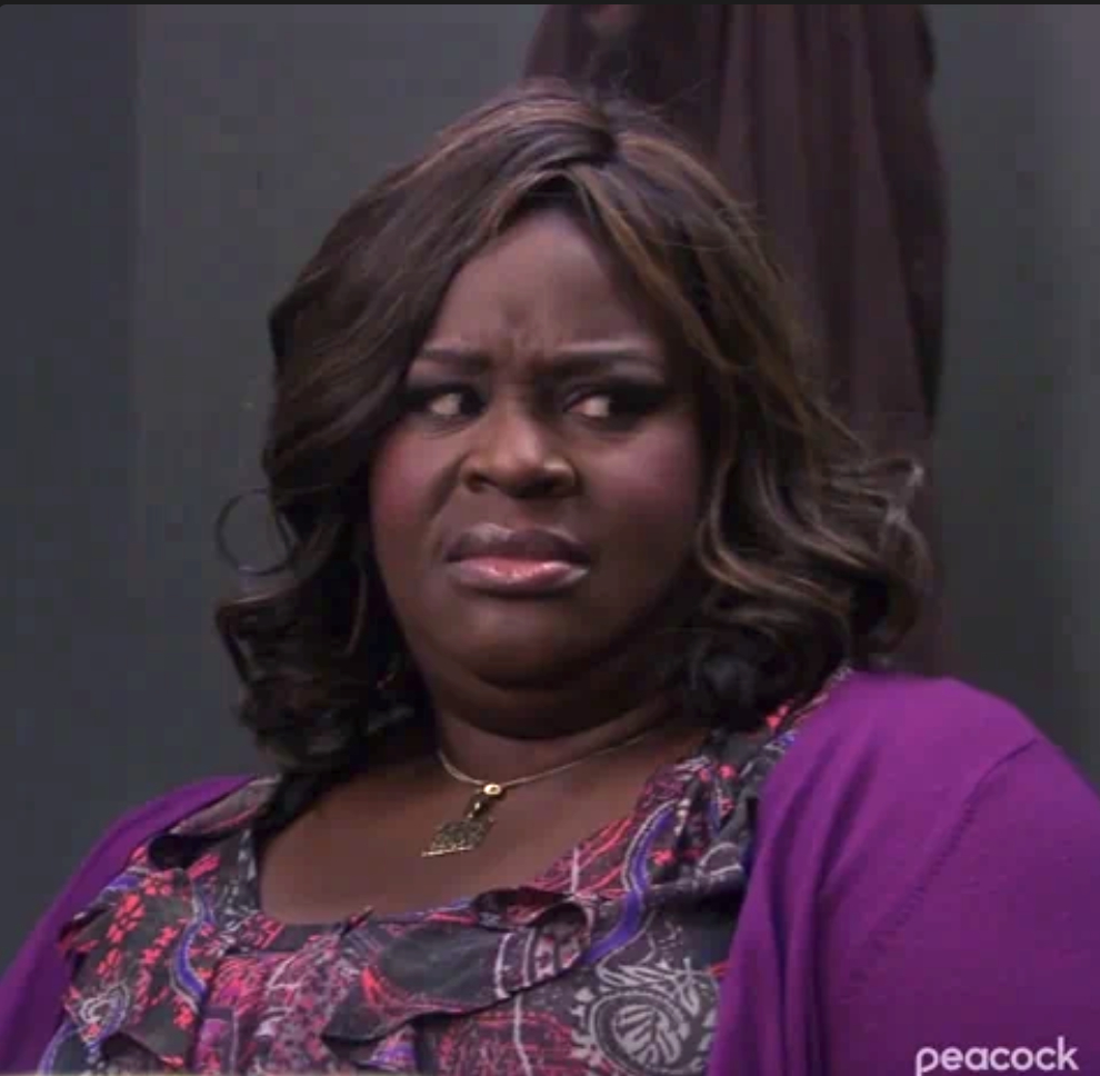 Retta, wearing a floral dress with a purple cardigan, has a skeptical expression in a scene from a TV show