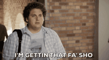 Jonah Hill says, "I'm gettin' that fa' sho'" in a scene from a movie, wearing a plaid shirt and graphic tee with a blurred background