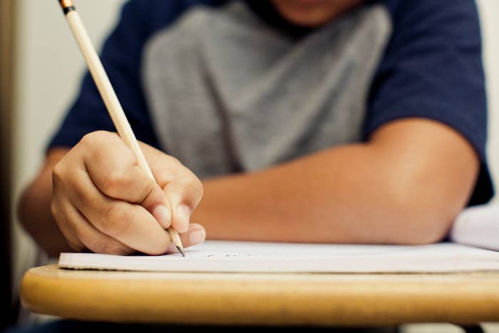 A child writing in a notebook at a desk, focusing on their work. The child's face is not visible