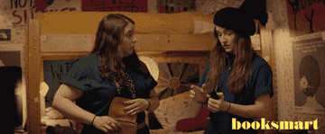 Beanie Feldstein and Kaitlyn Dever are in a bedroom, conversing. Beanie holds a bag, and Kaitlyn looks at a phone. The word "booksmart" is shown on the right