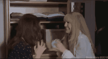 Anne Hathaway and Kate Hudson share a joyful moment, sitting together and smiling in a scene from "Bride Wars"