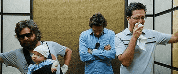 Zach Galifianakis holds a baby in a sling, Bradley Cooper stands with arms crossed, and Ed Helms wipes his nose in an elevator. Scene from "The Hangover."