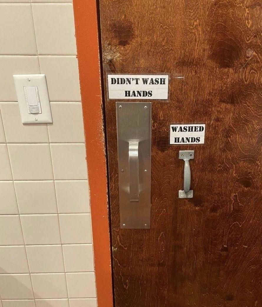 Photo of a restroom door with two signs near handles. One reads "Didn't wash hands" above a larger handle, and the other reads "Washed hands" above a smaller handle