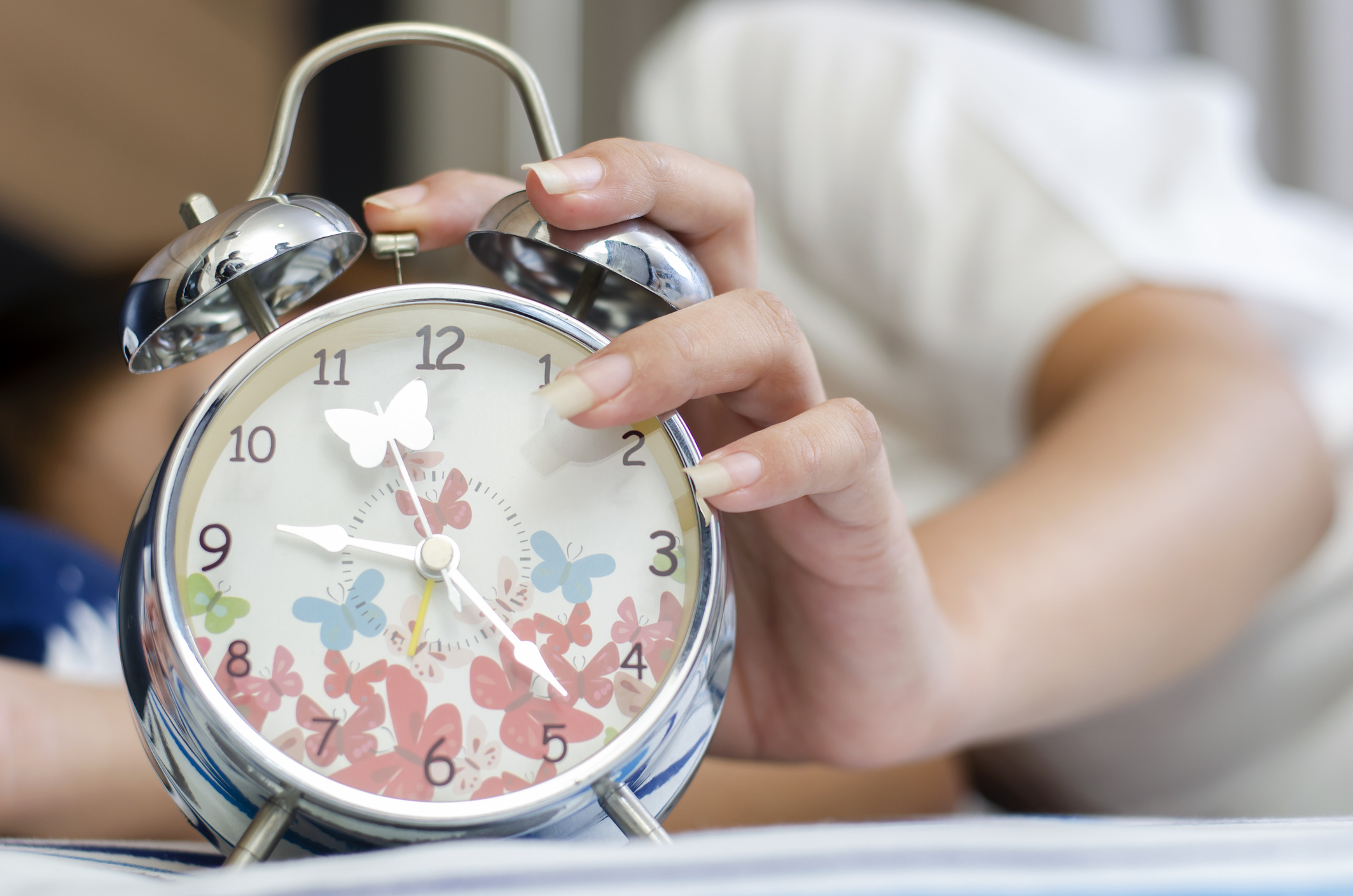 A hand reaches out to hit the snooze button on an analog alarm clock decorated with butterfly patterns, indicating the start of a new day