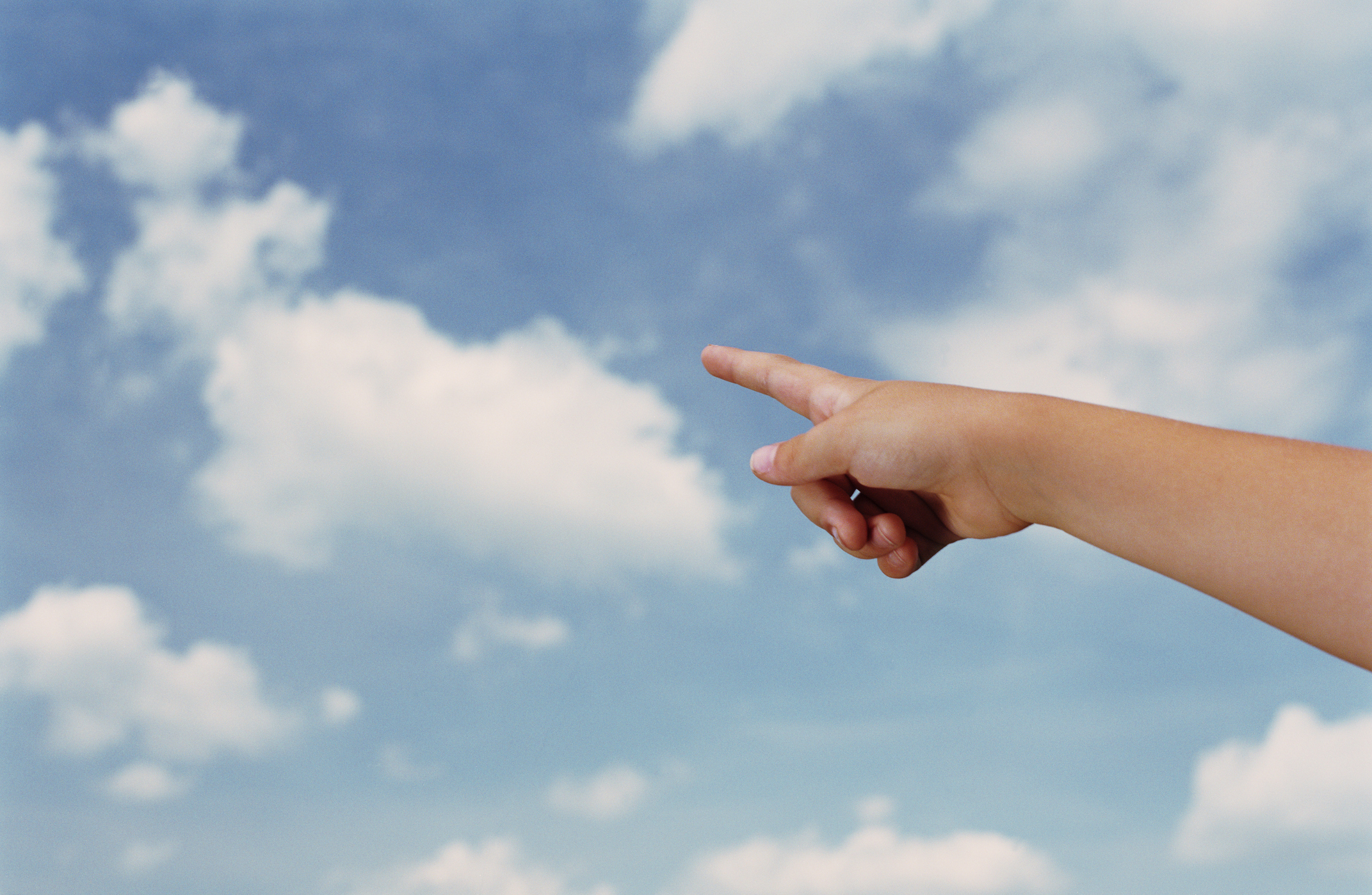 A child's hand points toward the clouds in the sky