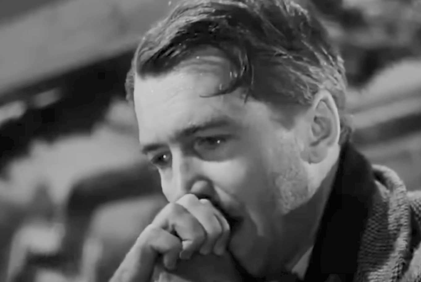 A pensive man with styled hair holds his hand to his face, appearing deep in thought