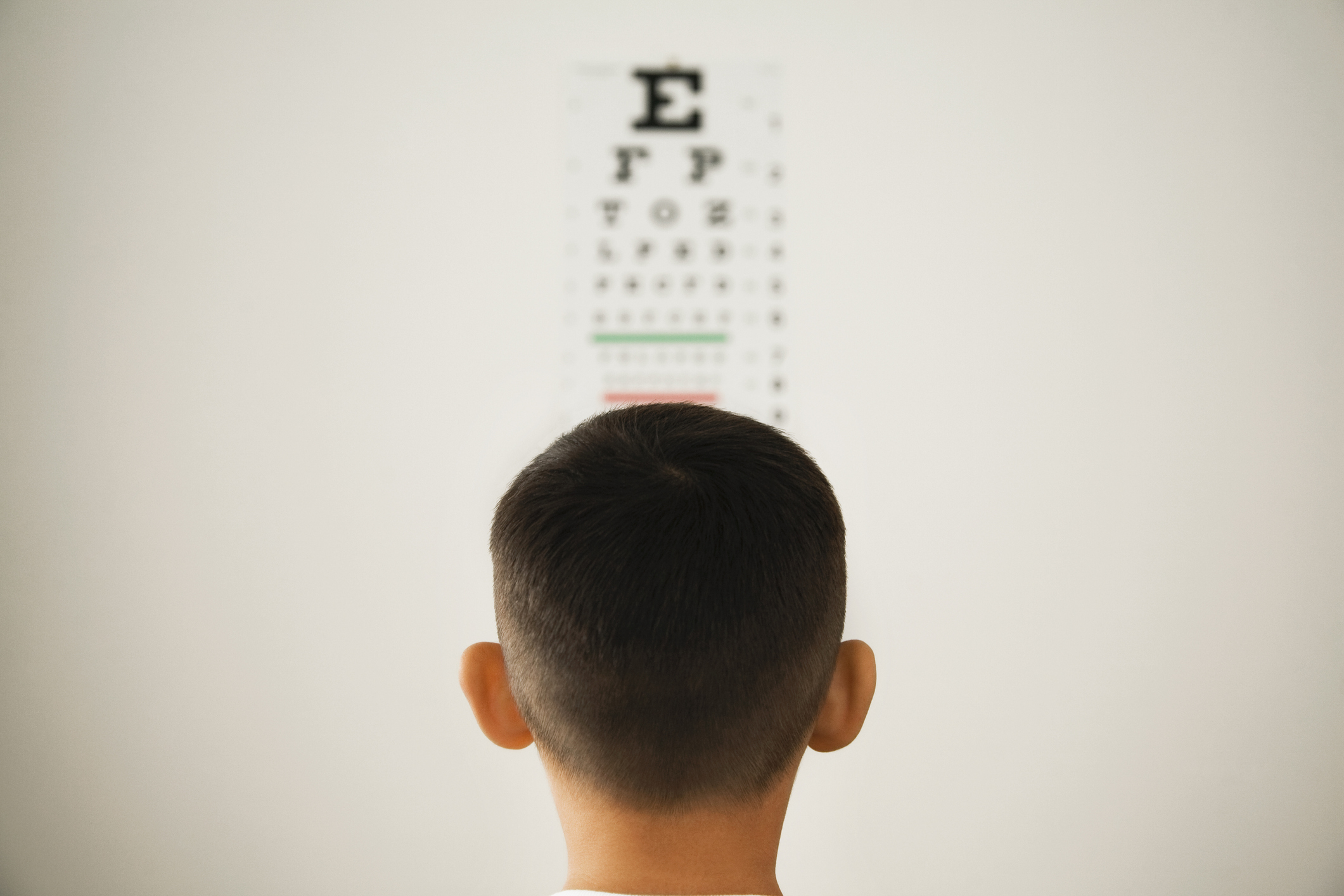 A child with short hair faces an eye chart on a wall for a vision test