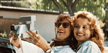 Susan Sarandon and Geena Davis as Thelma and Louise, smiling and taking a photo together. Text in the image reads "THELMA AND LOUISE"