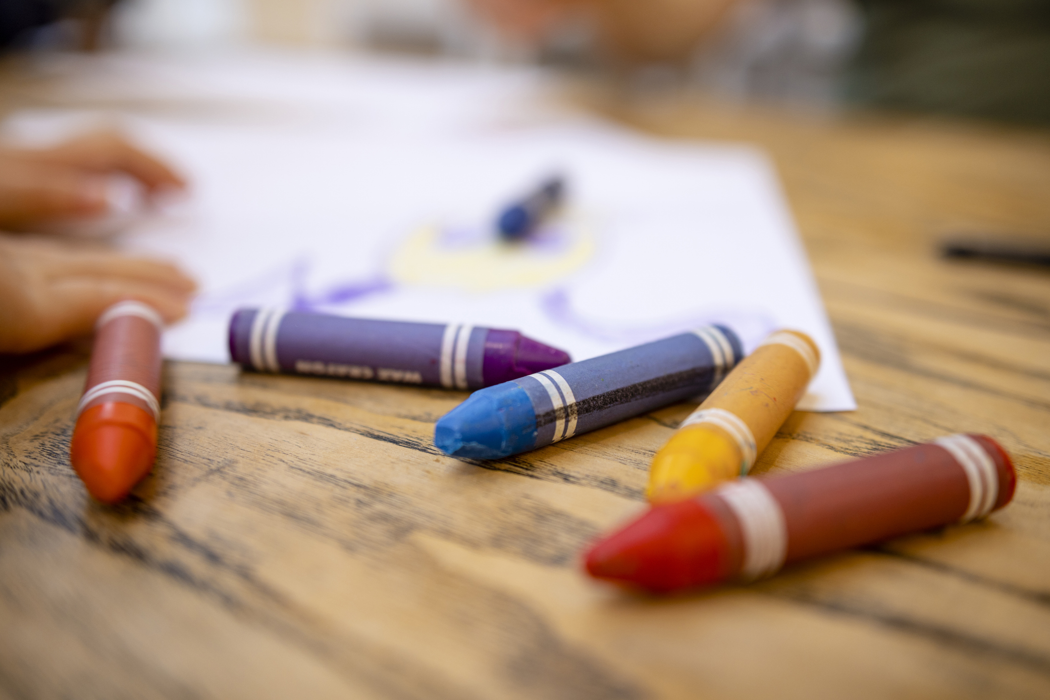 Children drawing with crayons on a table, hands visible holding and reaching for crayons