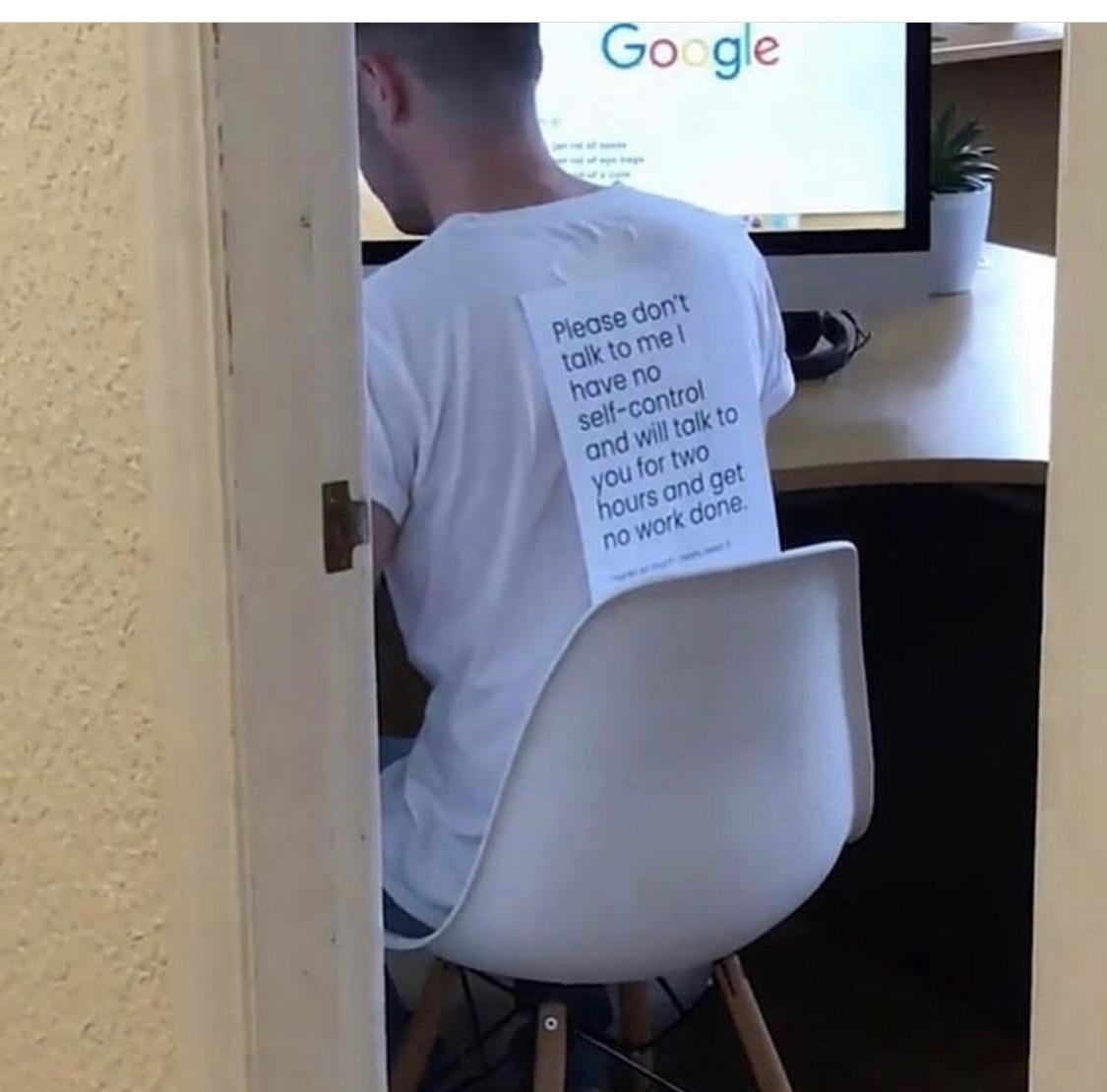 A person seated in front of a computer, wearing a shirt with text: "Please don't talk to me I have no self-control and will talk to you for two hours and get no work done."