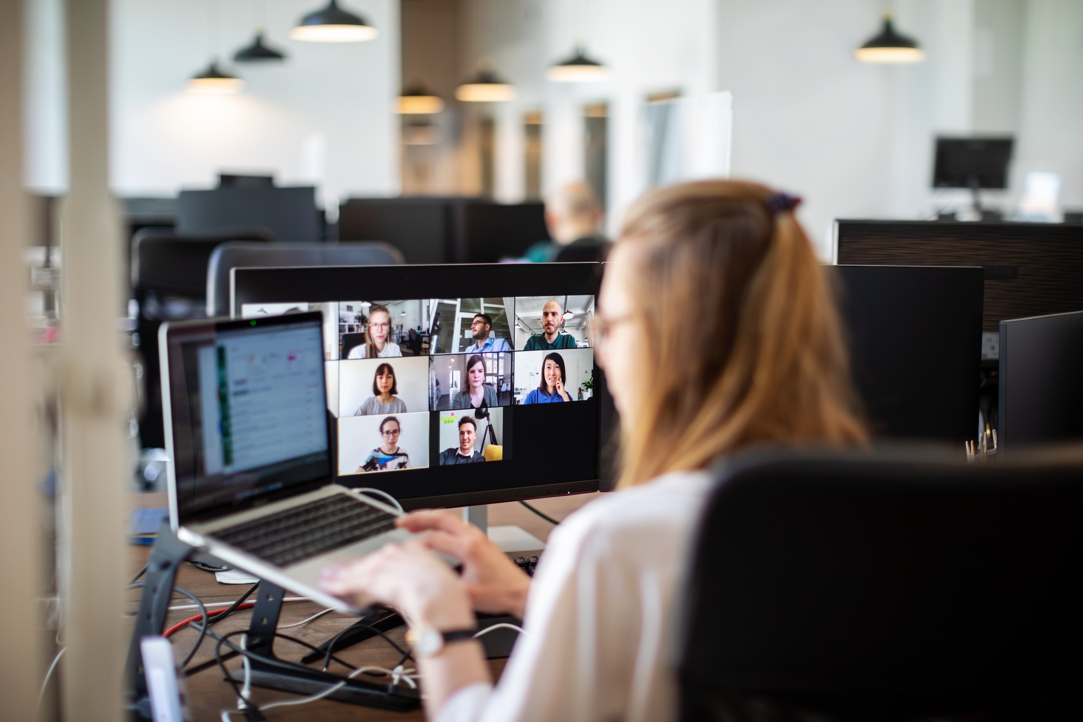 A person working on a laptop during a video conference call with multiple participants in an office setting
