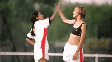 Keira Knightley and Parminder Nagra high-five each other on a soccer field. Keira is in a sports bra and shorts. Parminder is in a soccer uniform
