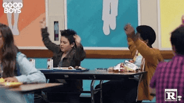 Good Boys movie scene: Two children, one in a jacket and the other in a brown sweater, dance excitedly at a school cafeteria table
