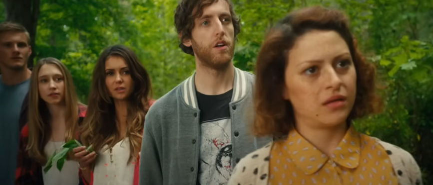 Five friends stand in a forest, looking surprised and confused