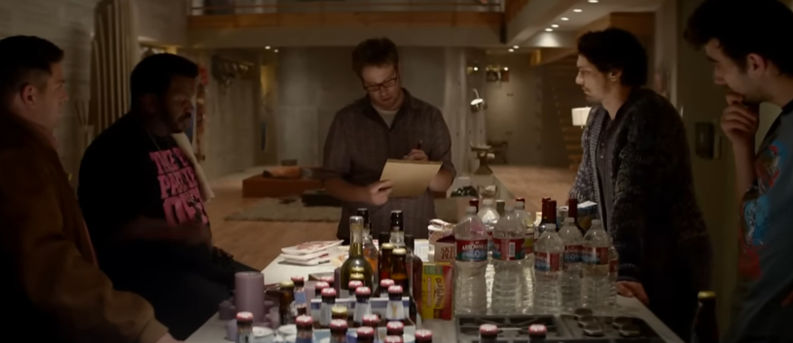 Five men stand around a table with various drinks and snacks, engaged in conversation