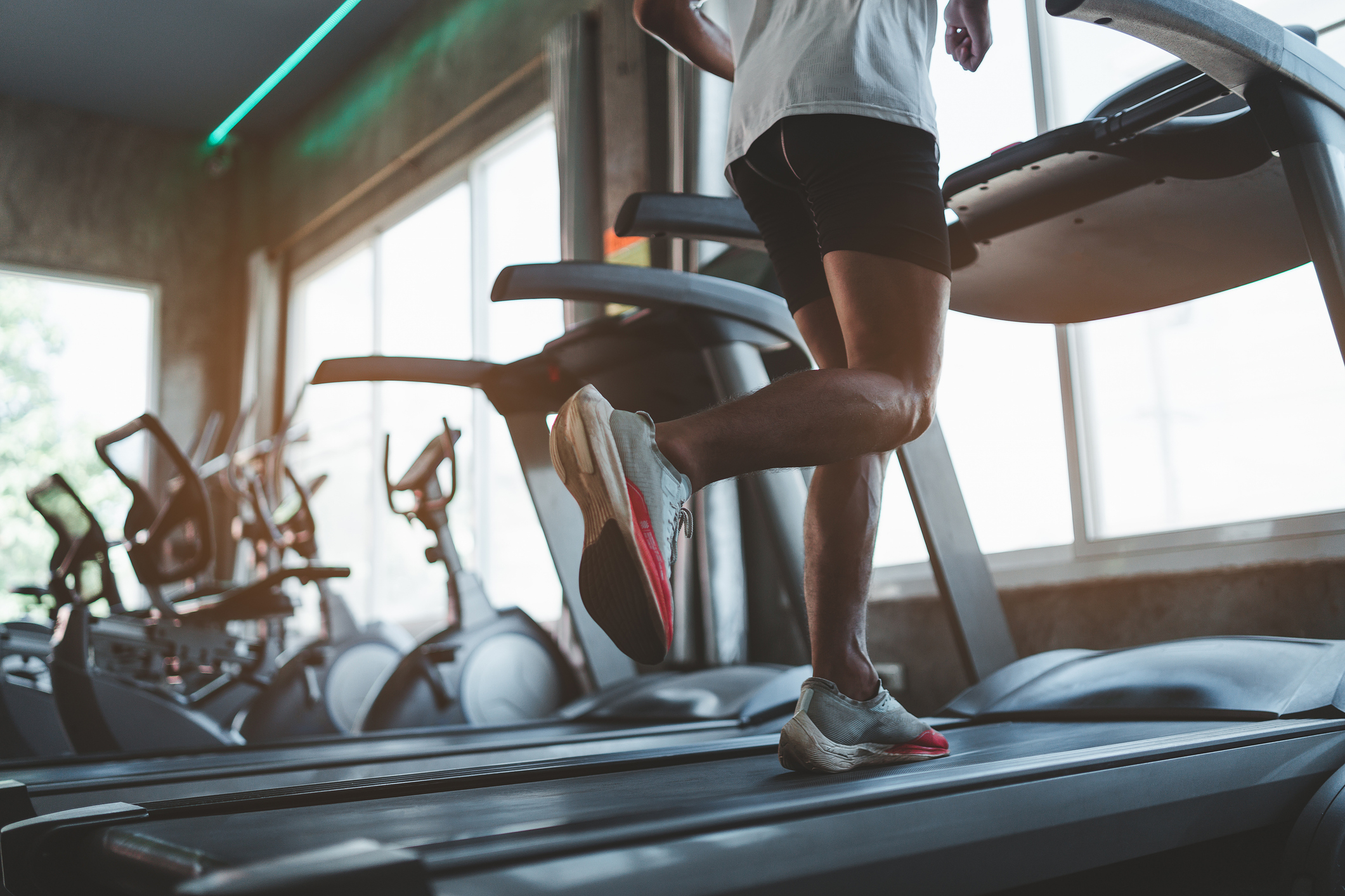 Person running on a treadmill in a gym with exercise bikes visible in the background