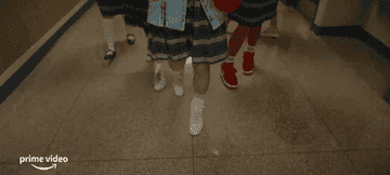 Group of students in school uniforms and sneakers walking down a hall.