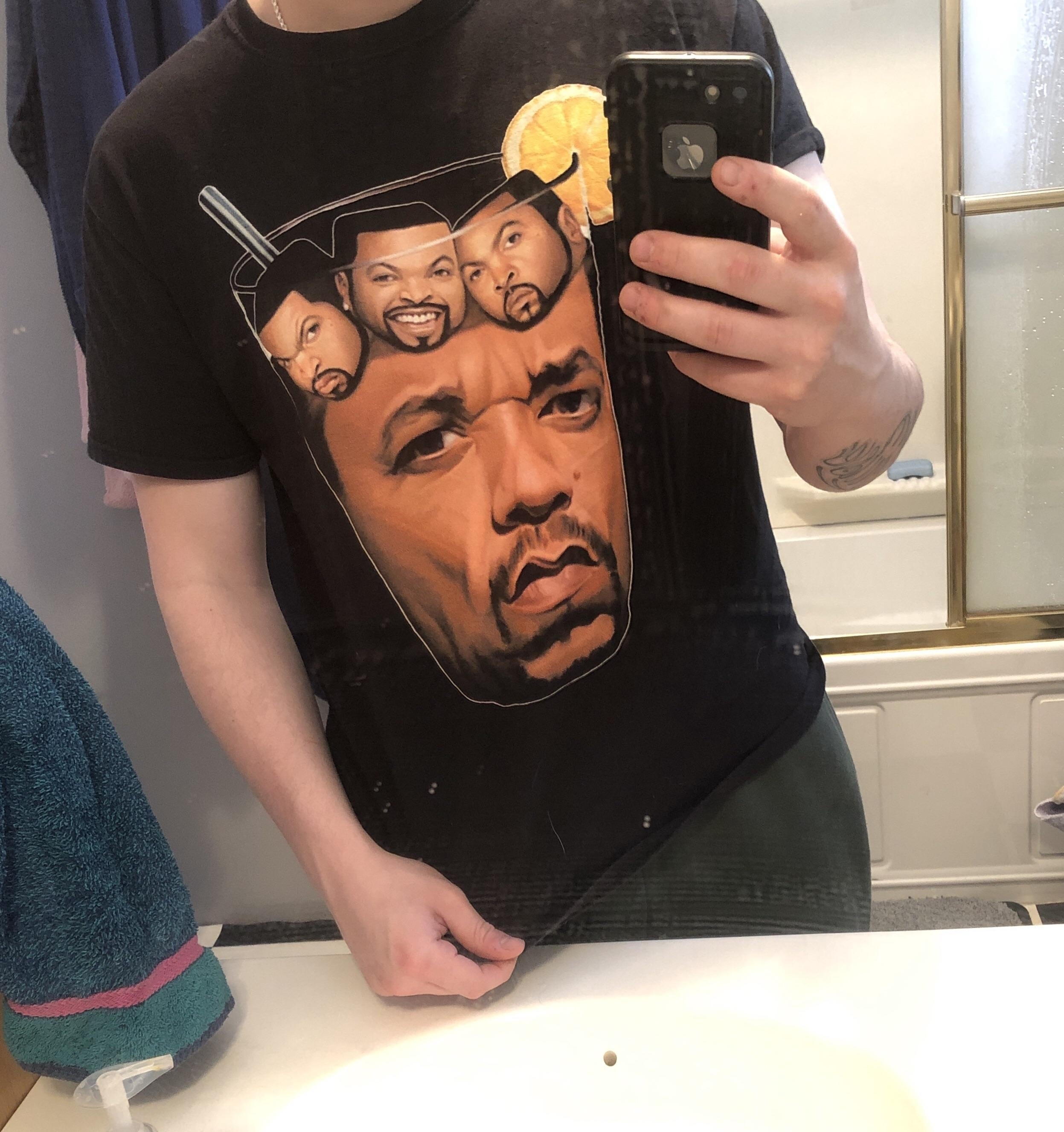 Person taking a mirror selfie wearing a t-shirt with a graphic featuring multiple faces of Ice Cube in a drink with a straw and lemon slice