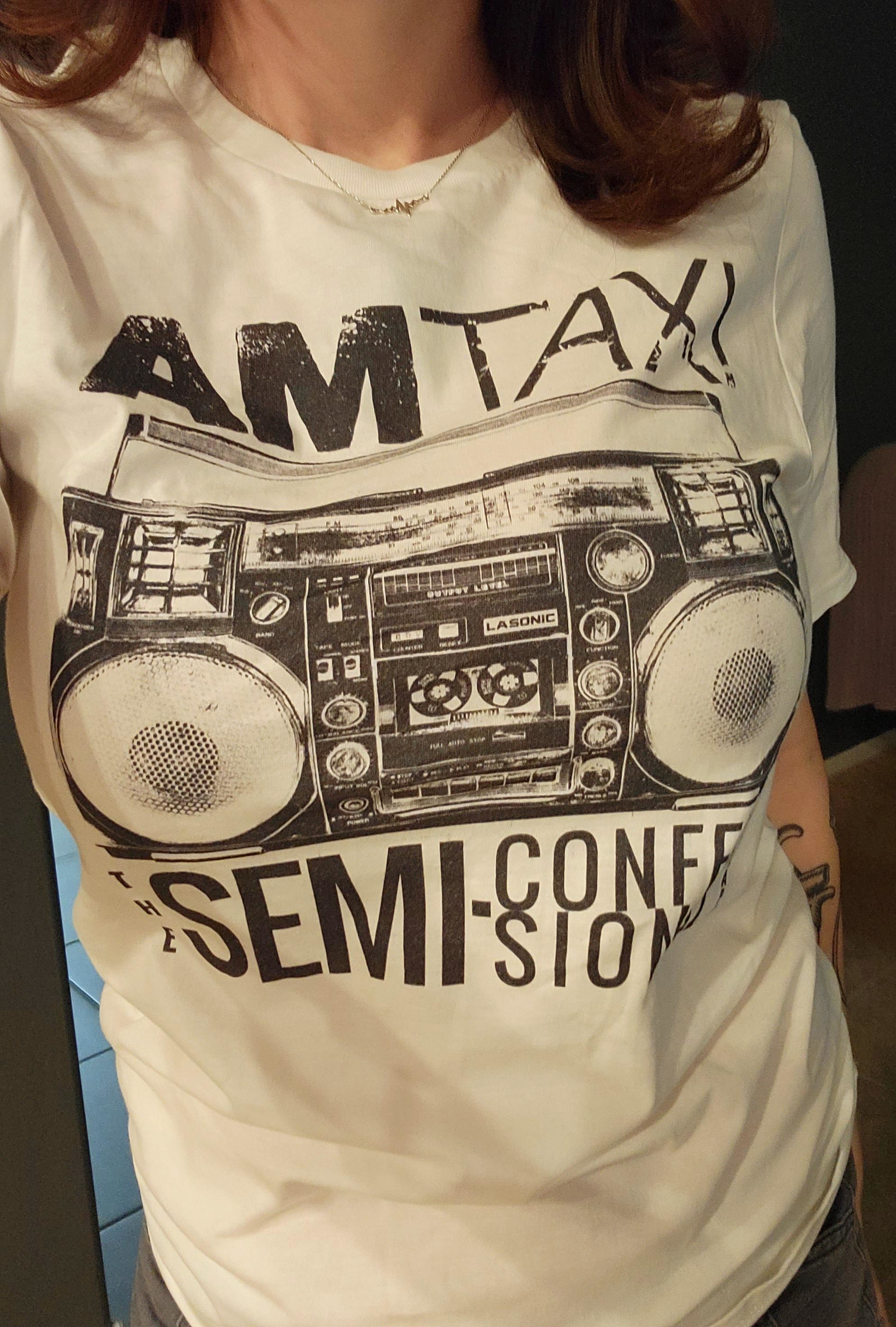 A person is wearing a T-shirt with a boombox print and the text "AM TAXI, The Semi-Confi-Sionist." Their face is not visible