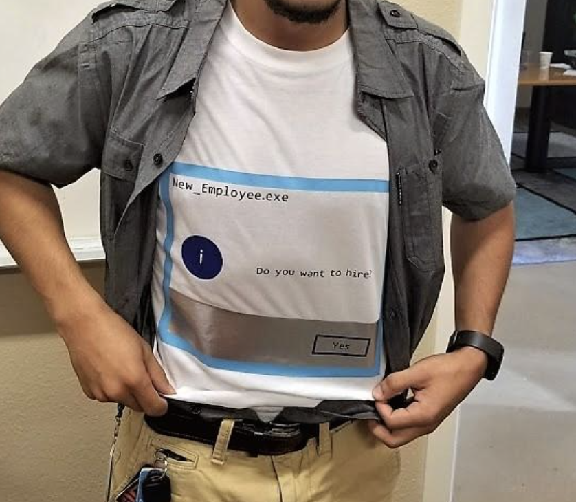 A person wears a shirt displaying a computer prompt, "New_Employee.exe. Do you want to hire?" with a "Yes" button. No names are provided