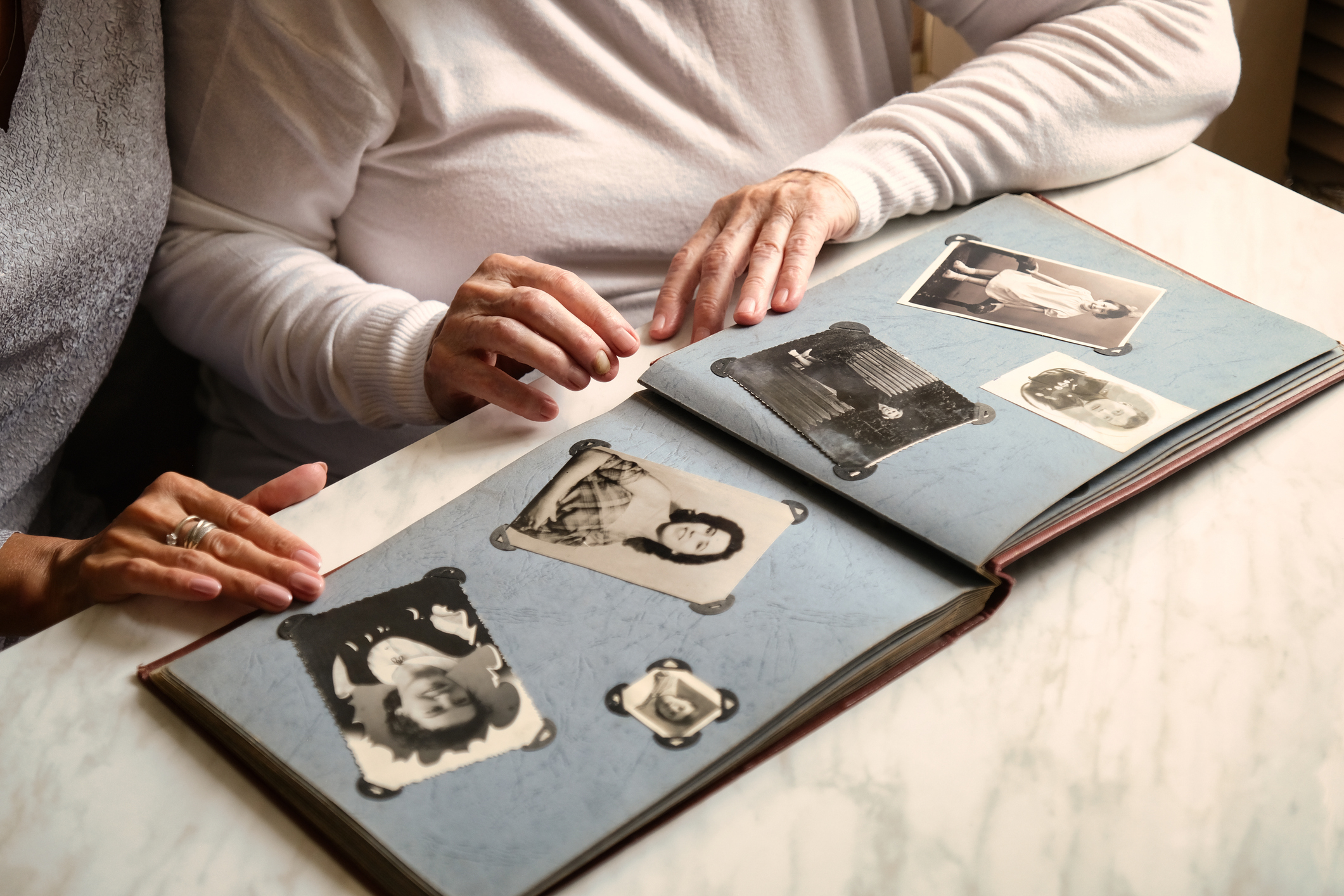 Two individuals are looking at an open photo album containing several black and white photographs, reminiscing together