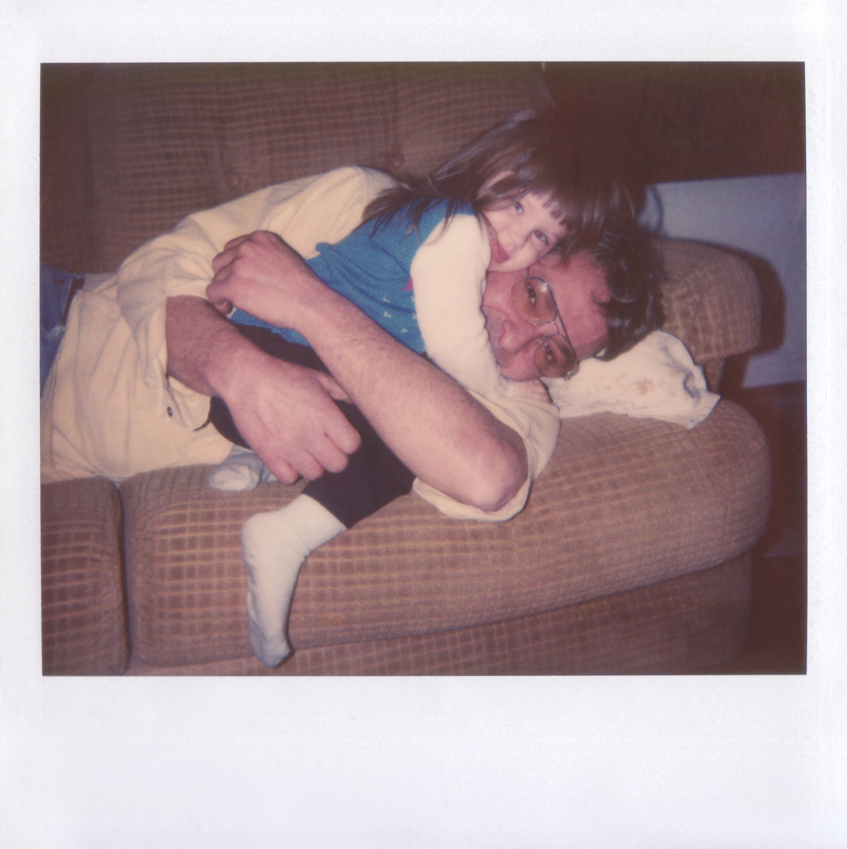 A young girl hugs a man laying on a couch, showing a loving and tender moment