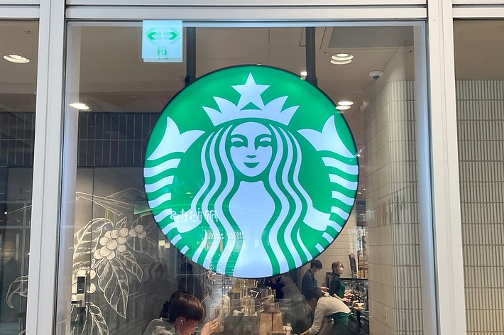 スターバックスのロゴが窓に描かれているカフェの風景。店内には数人の客が座っている。