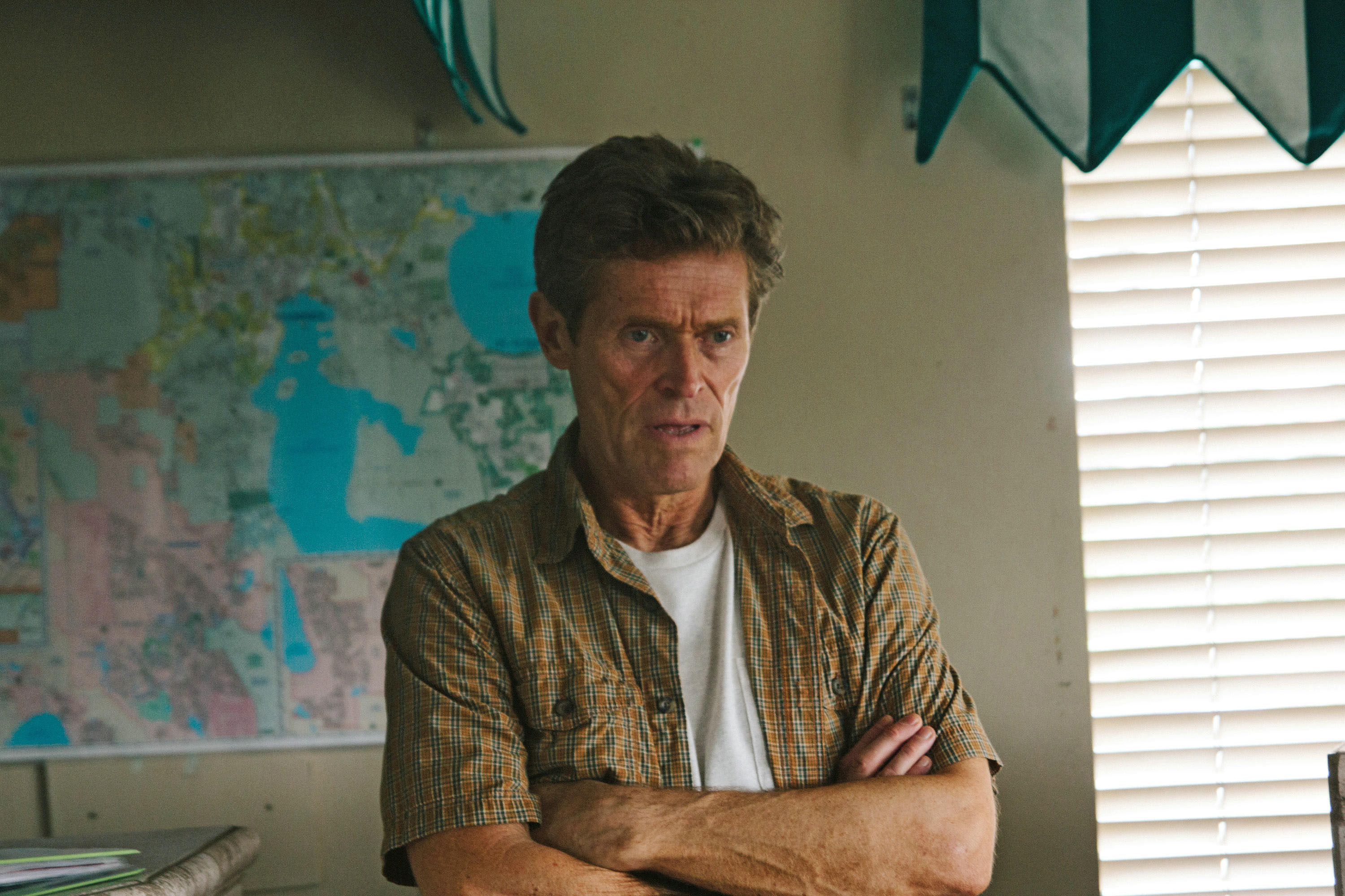 Willem Dafoe wearing a button-up short sleeve shirt with a map behind him in "The Florida Project"