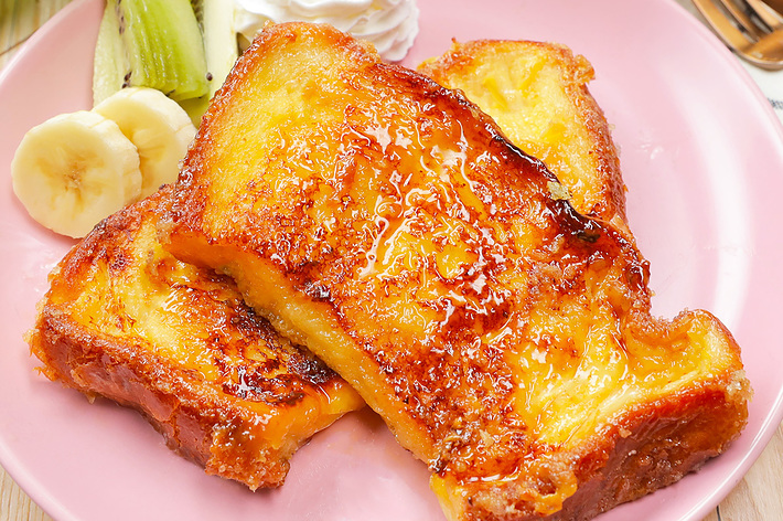 ピンクのプレートに盛り付けられたフレンチトースト、ホイップクリーム、キウイフルーツ、バナナ。