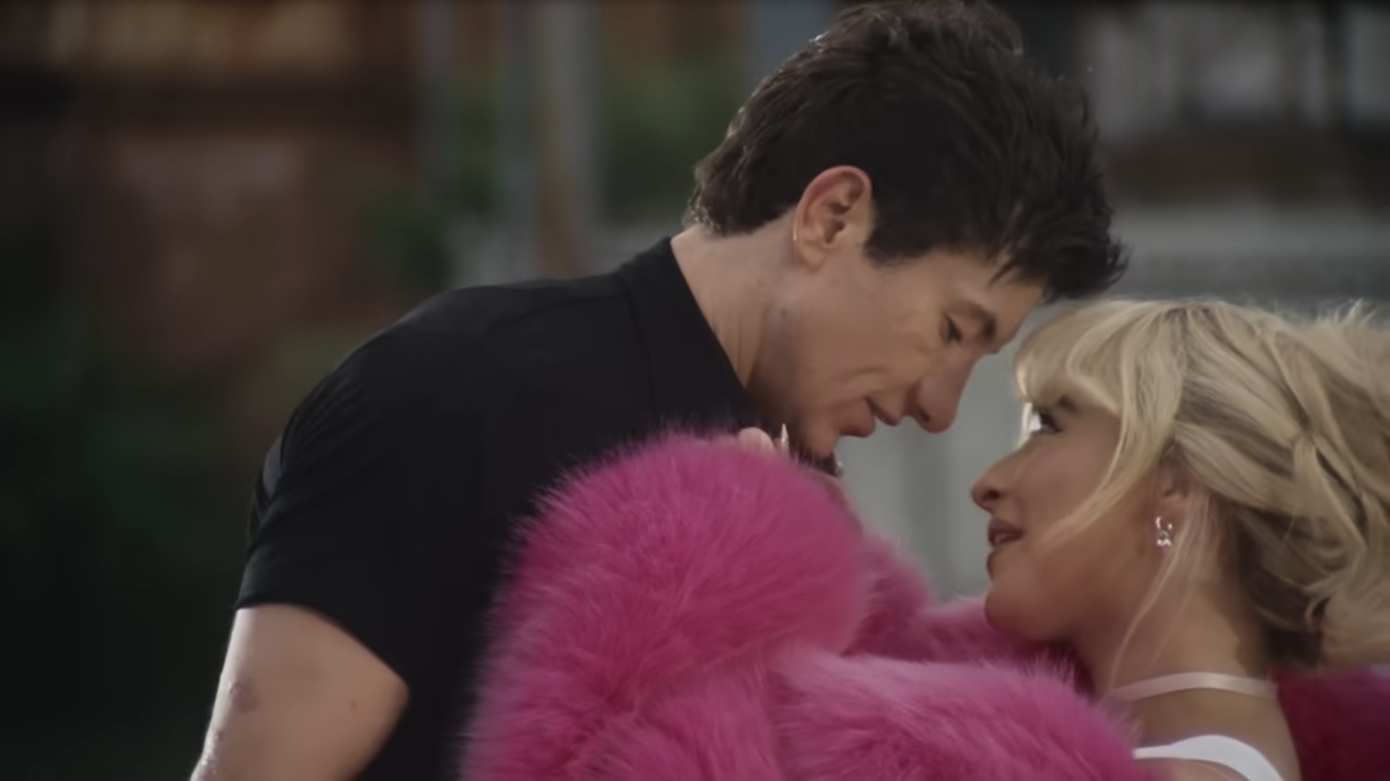 Barry Keoghan and Sabrina Carpenter share an intimate moment in the Please Please Please music video, with Barry leaning in towards Sabrina, who is wrapped in a fluffy garment