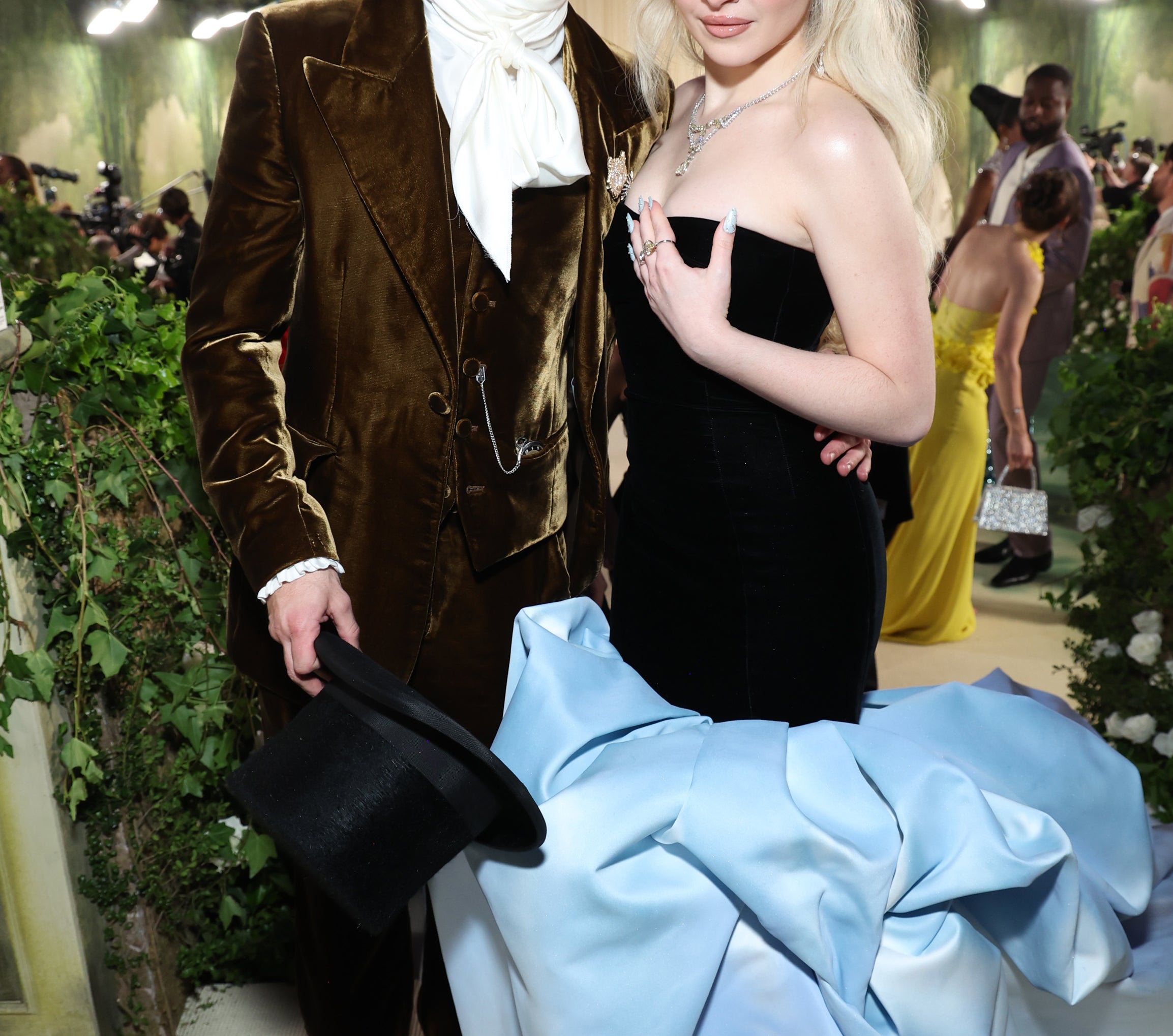 Barry Keoghan in a velvet suit and top hat and Sabrina Carpenter in an elegant strapless gown pose together at a formal event