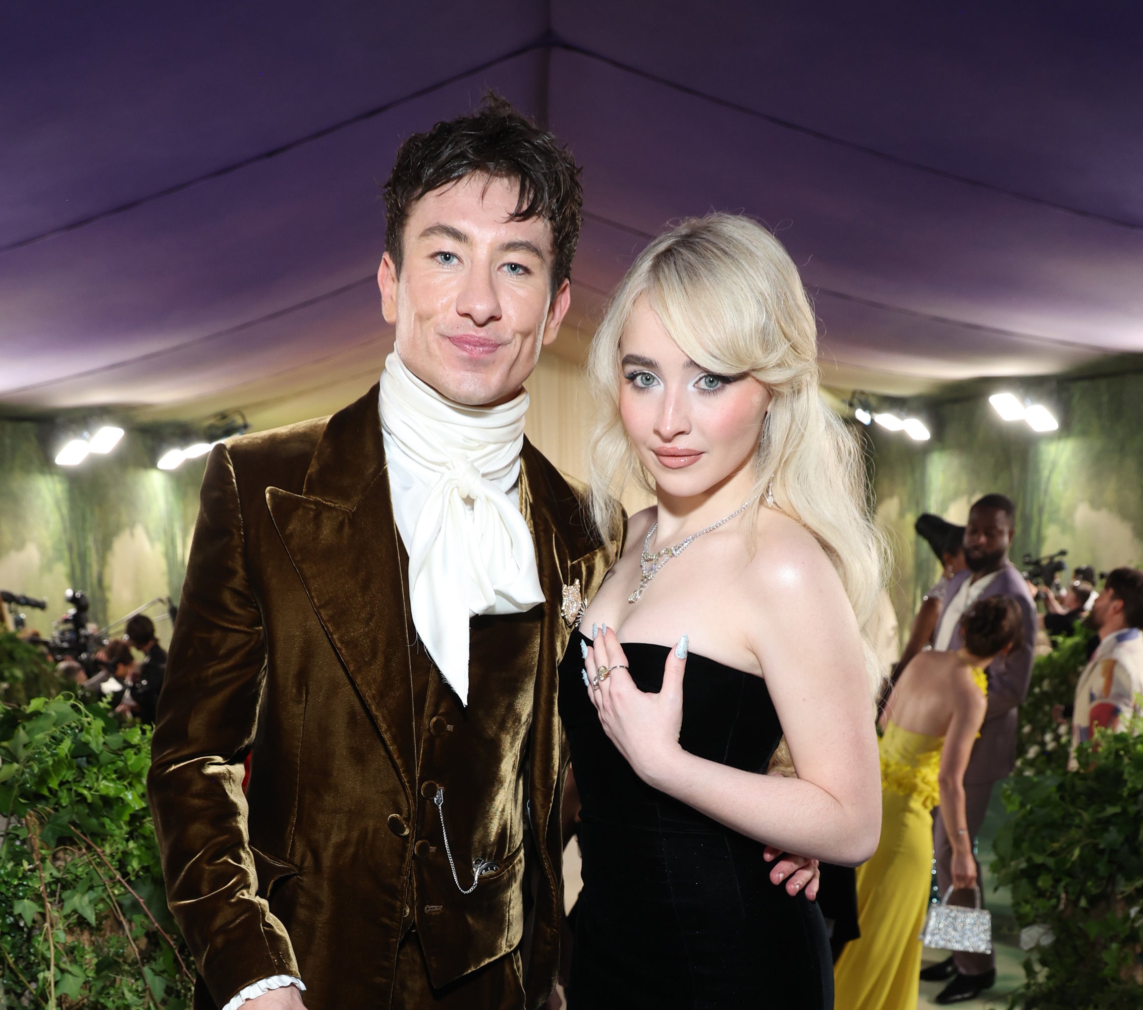 Barry Keoghan in a velvet suit and top hat and Sabrina Carpenter in an elegant strapless gown pose together at a formal event
