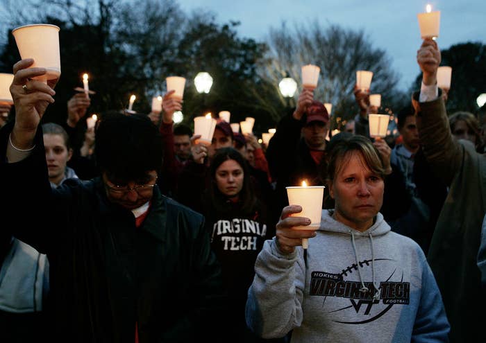 A group of people holding candles in a vigil, many wearing Virginia Tech apparel, likely commemorating an event related to the university