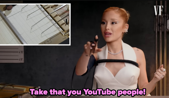 Ariana Grande wears a glamorous white dress, holding a polygraph machine sensor, with text "Take that, you YouTube people!" in pink at the bottom
