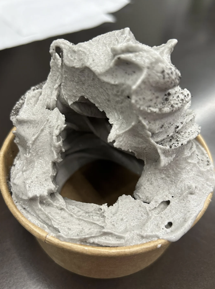 A cup of grey-colored soft-serve ice cream with a smooth, swirling texture