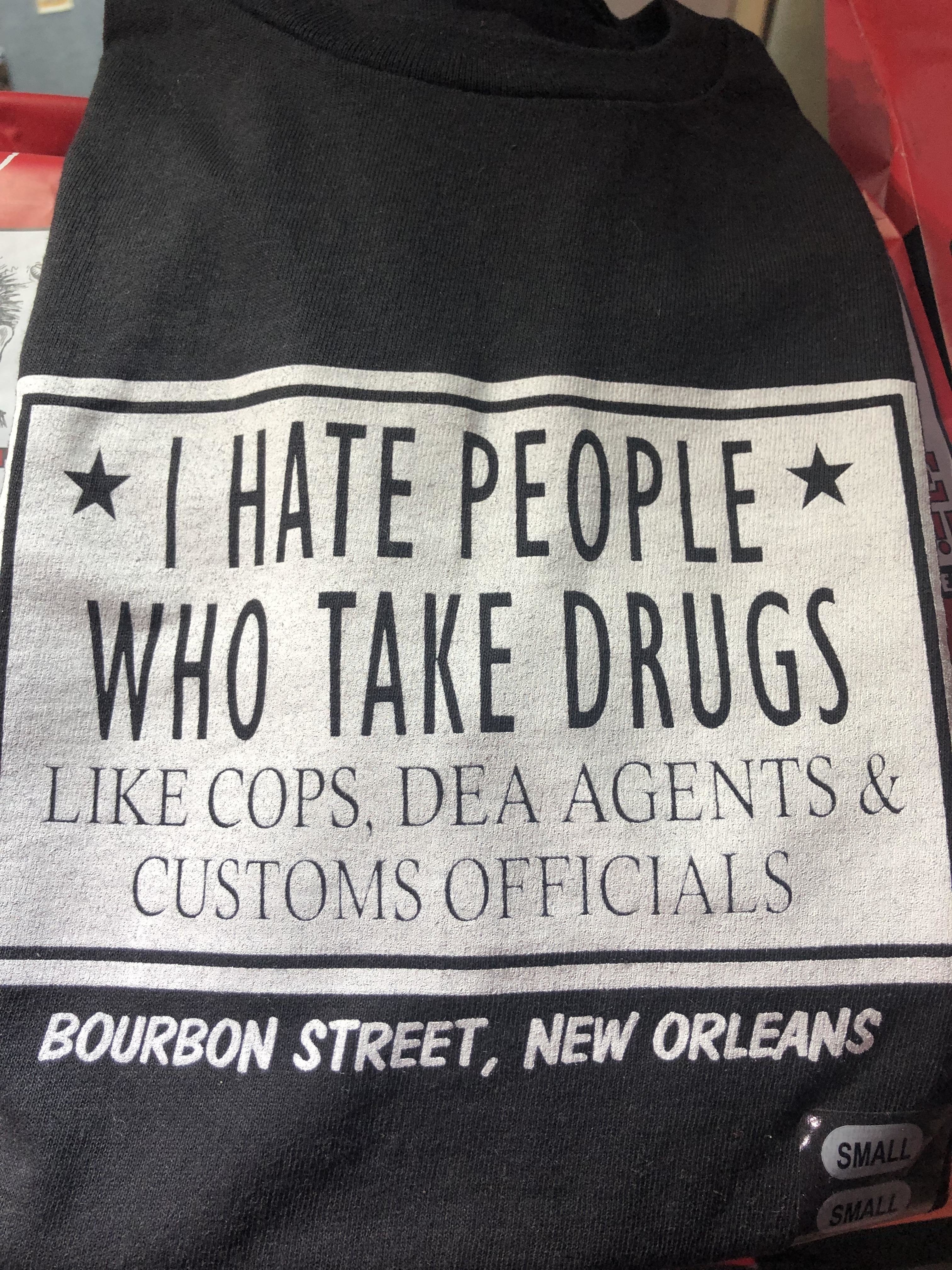 A t-shirt reads: "I HATE PEOPLE WHO TAKE DRUGS LIKE COPS, DEA AGENTS & CUSTOMS OFFICIALS. BOURBON STREET, NEW ORLEANS."